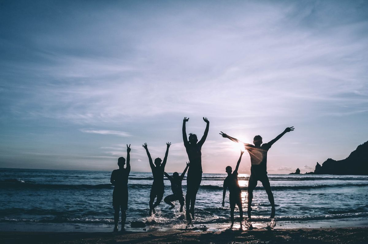 A Group Of People Standing On A Beach With Their Arms Raised