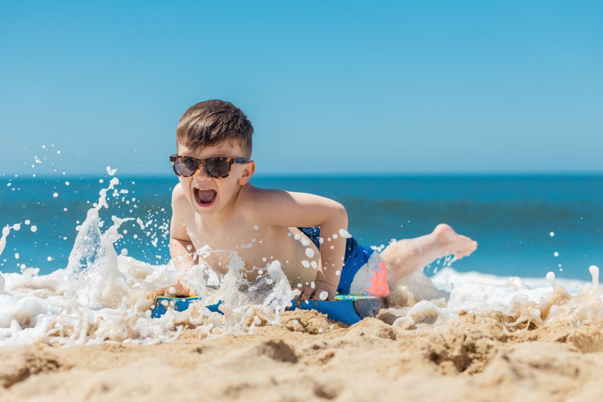 A Boy In Sunglasses Playing In The Sand At The Beach