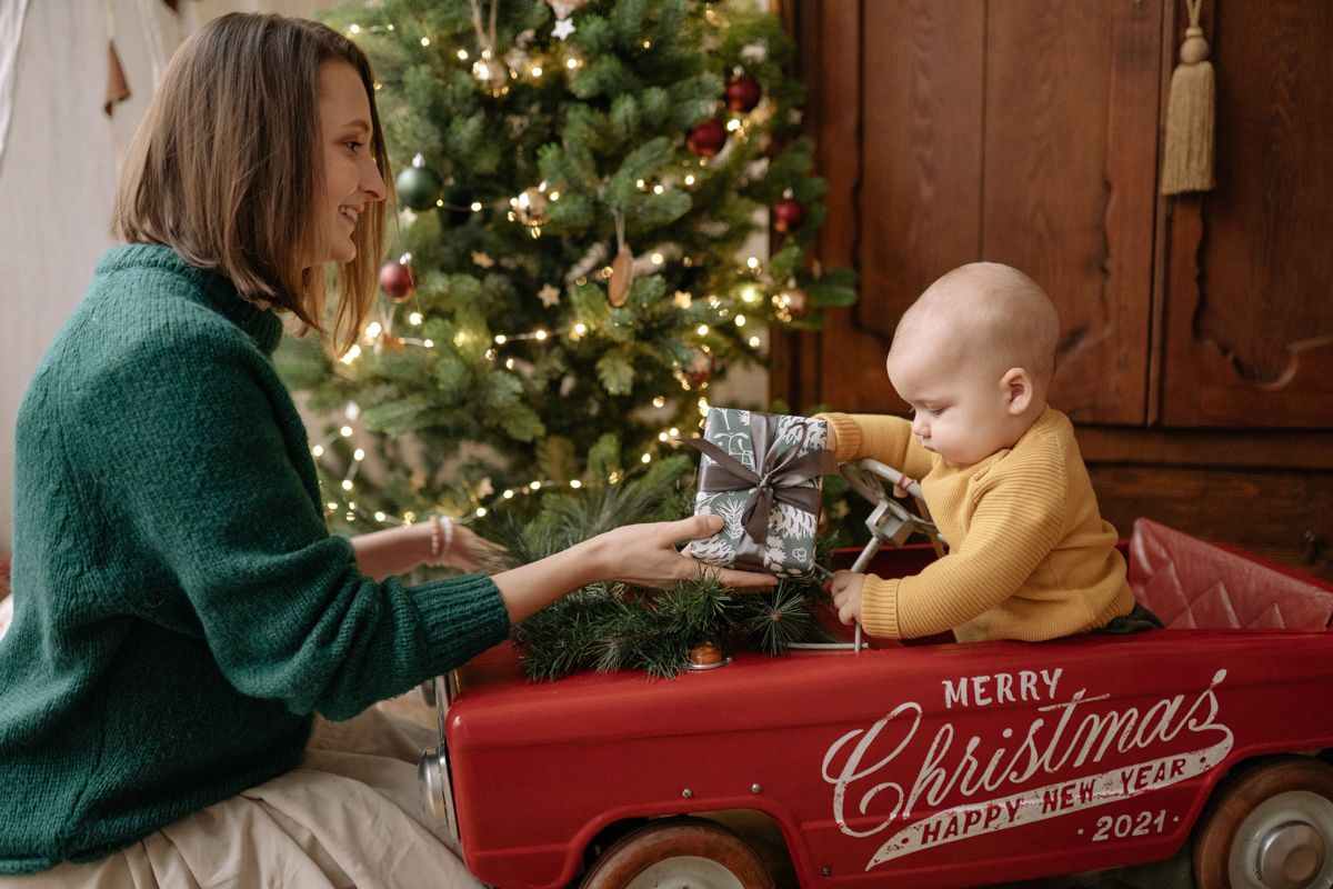 A Person And A Baby In A Red Car By A Christmas Tree