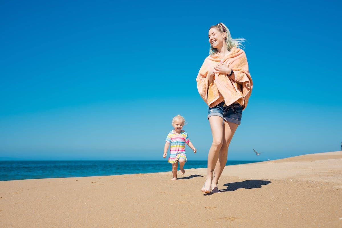 A Woman And A Child Walking On A Beach