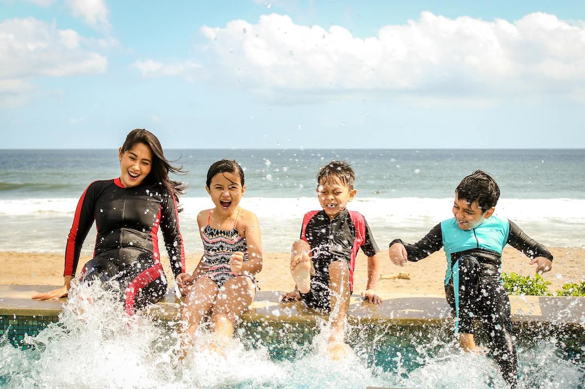 A Group Of Children In Wet Suits Running In The Water