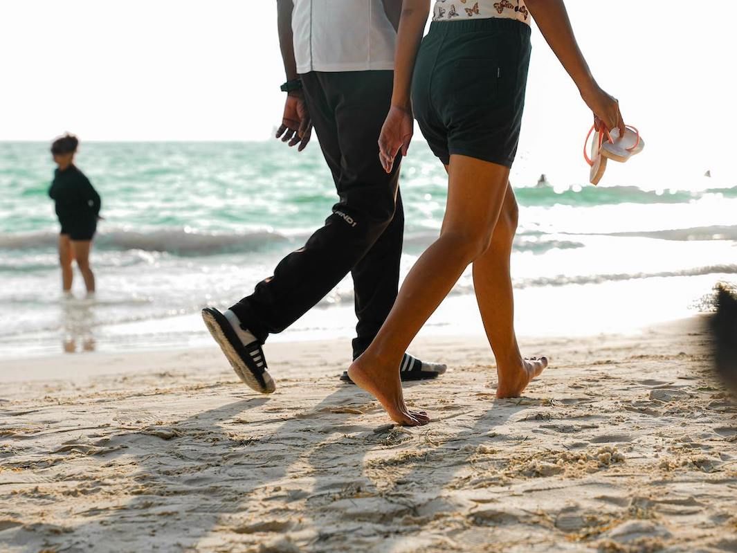 A Pair Of People Walking On A Beach