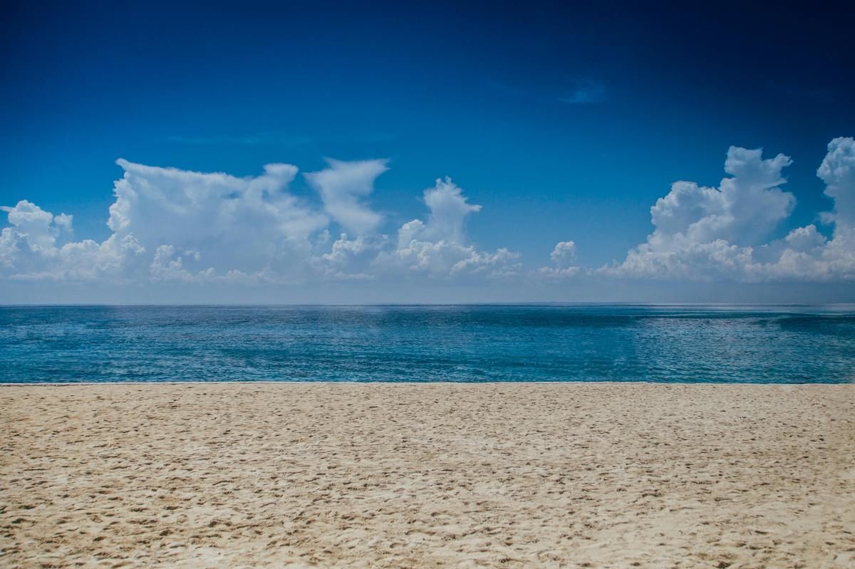 A Sandy Beach With Blue Water And Clouds In The Sky