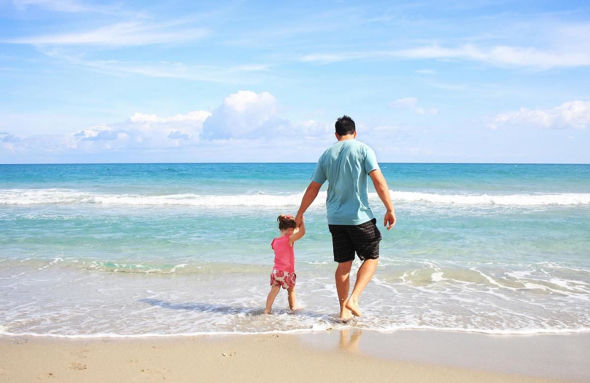 A Man And A Child Walking On A Beach